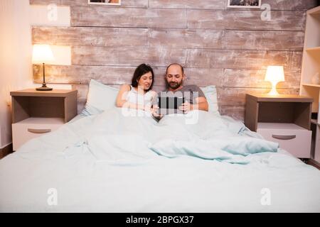 Sposato coppia caucasica indossando pigiami utilizzando un tablet computer prima di dormire. Foto Stock