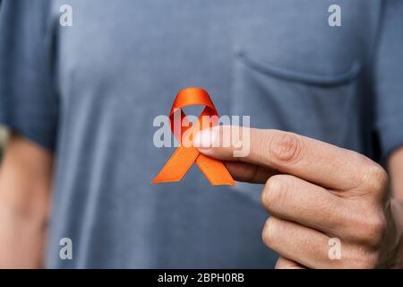 primo piano di un giovane caucasico con un nastro arancione in mano, a sostegno delle persone affette da sclerosi multipla Foto Stock