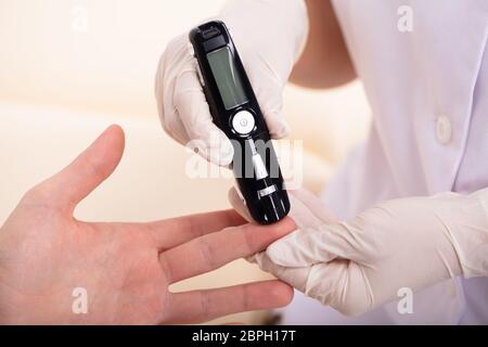 Close-up di un medico mano la misurazione del sangue del paziente a livello di zucchero con il glucometro Foto Stock