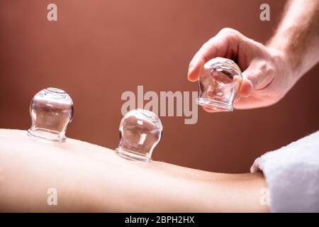 Close-up del terapeuta maschio immissione trasparente bicchieri in vetro su una donna indietro Foto Stock