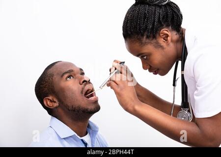 Medico donna Controllo dell'uomo mal di gola con abbassa lingua su sfondo bianco Foto Stock