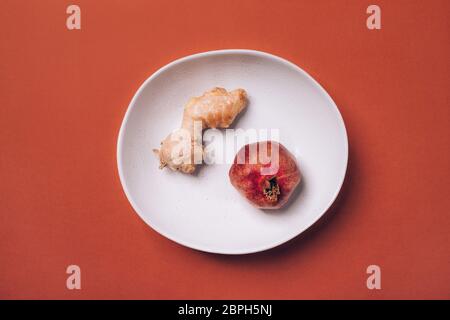 Melograno maturo e radice di zenzero su un piatto su fondo rosso-arancio. Foto Stock