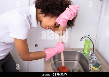 Stanco chi indossa guanti rosa pulizia lavello riempito con acqua con tazza di stantuffo Foto Stock