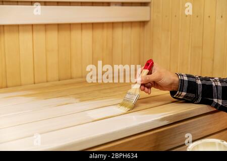 mano che applica cera protettiva per legno sul banco sauna con pennello Foto Stock