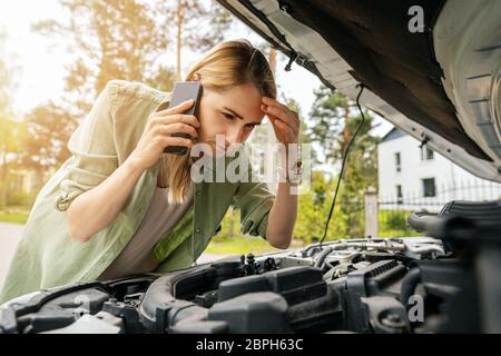 donna che guarda il motore dell'auto rotto e parla al telefono Foto Stock