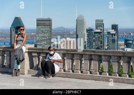 Montreal, CA - 18 Maggio 2020 : due giovani donne che indossano la maschera facciale tra l'epidemia di coronavirus e lo skyline di Montreal sullo sfondo Foto Stock