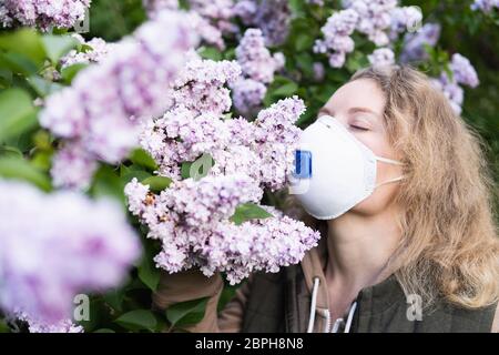 La giovane bionda puzza di lilla attraverso il respiratore FFP2. Immagine concettuale della quarantena e dell'allergia del virus corona. Foto Stock