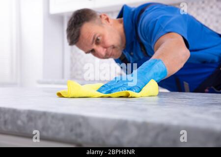 La sezione centrale di un maschio bidello sporca la pulizia della cucina con la bottiglia spray e igienico Foto Stock