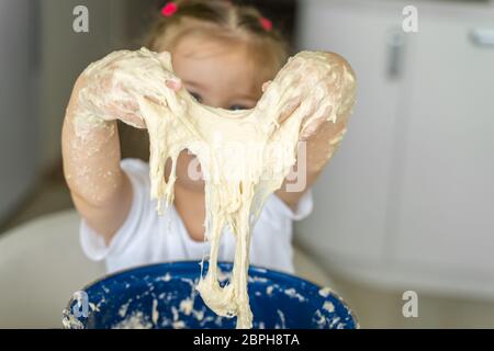 3-4 anni ragazza impasta lievito impasto in una padella blu, mani closeup. tempo libero per la famiglia Foto Stock