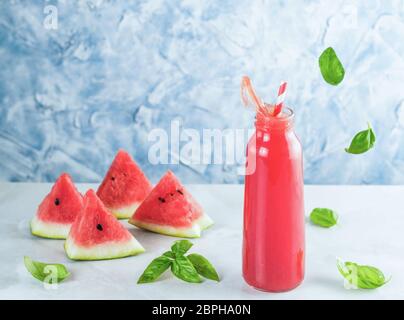 Appetitosi gustosi drink di anguria con basilico in una bottiglia di vetro sulla tabella grigia. In casa di anguria e basilico limonata con spruzzi. Copia dello spazio. Affettare wa Foto Stock