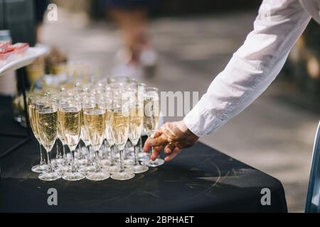 Molti bicchieri con champagne sono sul tavolo. Il tavolo è coperto da una tovaglia bianca. L'uomo prende un bicchiere di champagne Foto Stock