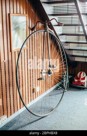 Bicicletta in stile antico con una ruota grande e una piccola sotto le scale in una casa. Foto Stock