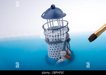 Spazzola di pittura e modello piccolo faro posto in acqua blu Foto Stock