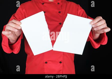 Uomo in un rosso mantiene uniforme di un foglio bianco di carta strappata a metà, sfondo nero Foto Stock