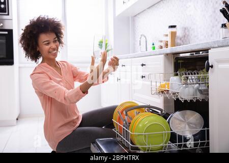 Felice giovane donna controllo lavato trasparente vetro potabile vicino la lavastoviglie Foto Stock