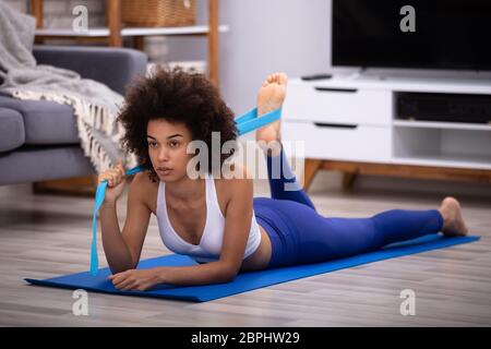 Grave giovane donna in abbigliamento sportivo facendo allenamento con cinghia di Yoga a casa Foto Stock