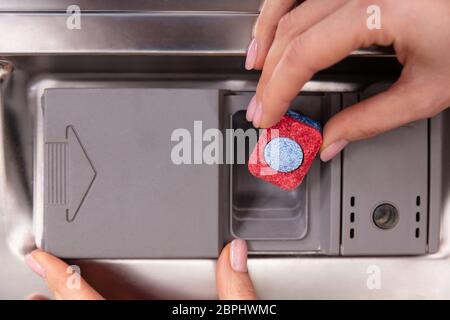 Mano umana mettendo il rosso e il blu di sapone colorato compressa nella fessura di lavastoviglie Foto Stock