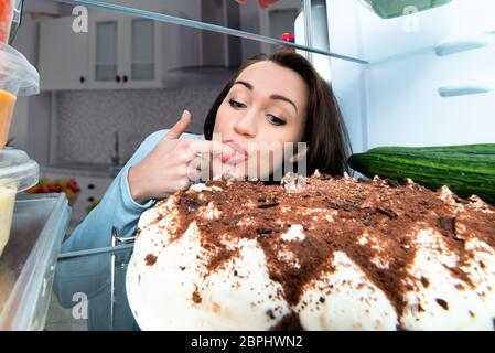 Giovane donna Torta di degustazione con il dito in bocca Foto Stock