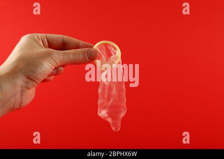 Close up man mano che tiene una aperta del condom in lattice su sfondo rosso con copia spazio, basso angolo vista laterale Foto Stock