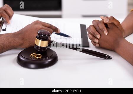 Close-up di un giudice che spiega il contratto per il suo cliente con martello e anelli d oro Foto Stock