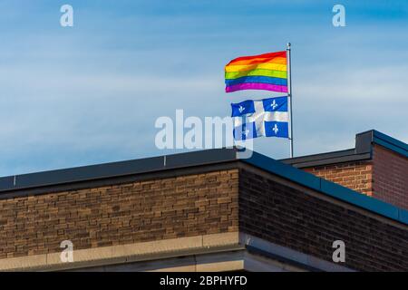 Bandiera gay iridata e bandiera del Quebec che sventolano nel vento sul tetto di un edificio a Montreal, Canada Foto Stock