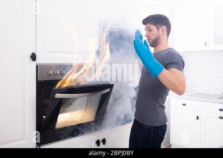 Paura giovane uomo Guardando il fuoco che esce dal forno in cucina Foto Stock