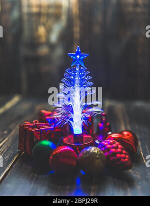 Piccolo albero di Natale LED illuminazione intorno con piccolo ornamento di Natale sullo sfondo di legno scuro tavolo. Foto Stock