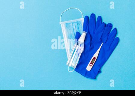 Vista dall'alto dei guanti in lattice, bottiglia di igienizzante per mani imbevuto di alcool, maschera medica e termometro digitale su sfondo blu. Protezione contro il virus antibatterico co Foto Stock