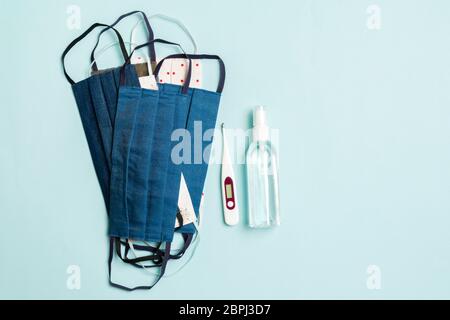 Vista dall'alto di maschere in cotone fatte a mano, termometro digitale e igienizzatore con gel di alcol su sfondo blu. Concetto di equipaggiamento protettivo con spazio per copia. Foto Stock