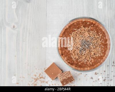 Cioccolato budino di chia in vetro e cubetti di cioccolato slice grigio su un tavolo di legno. Vegano sana colazione con copia spazio. Vista superiore o flat-lay. Foto Stock