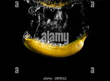 Banana caduta in acqua con splash su sfondo nero. Foto Stock