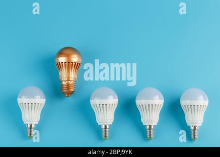 La lampadina oro è più alta e si distingue da una fila di lampade bianche su sfondo blu. Il concetto di pensiero non standard, leadership e differenze Foto Stock