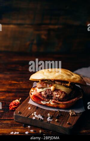 Cheeseburger con carne di manzo Patty, Wisconsin il formaggio svizzero, prosciutto, funghi saltati, Dijon senape, maionese e rotolo di patate. Orientamento verticale e copia Foto Stock