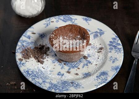 Torta al cioccolato al coulant al forno servita con scaglie di cioccolato e zucchero a velo su un piatto su un tavolo di legno. Foto Stock