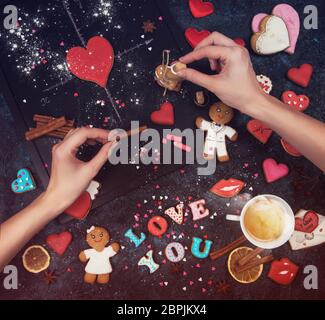 Mani femminili che decorano la composizione di pan di zenzero di amore. Pani di zenzero per San Valentino o tema di nozze. Foto Stock