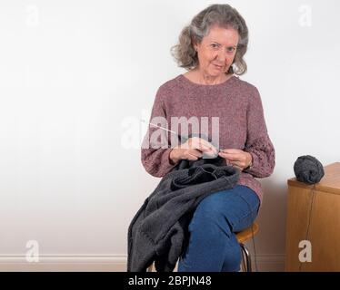 Donna che indossa un ponticello a maglia a mano che indossa un ponticello grigio in lana e guarda la fotocamera, sfondo bianco Foto Stock