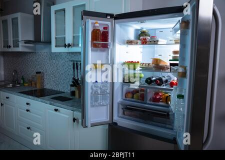 Un frigorifero aperto pieno di frutta, succo di frutta e verdure fresche in cucina Foto Stock