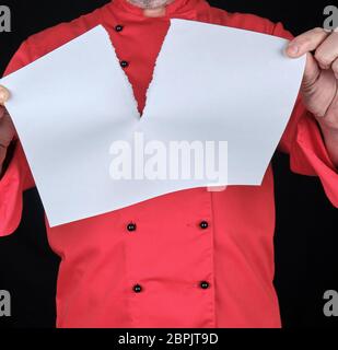 Chef in rosso uniforme tenendo un vuoto del foglio bianco e lo strappo a metà, sfondo nero Foto Stock