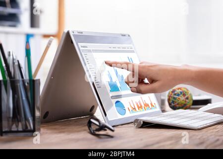 Close-up di una imprenditrice di puntamento a mano su schermo di computer portatile che mostra il grafico sopra la scrivania in legno Foto Stock