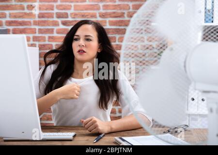 Giovane imprenditrice stessa di raffreddamento nella parte anteriore della ventola durante il tempo caldo in ufficio Foto Stock