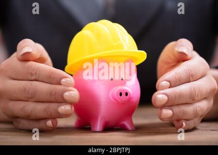 Close-up di mano di una persona di colore rosa di protezione Salvadanaio con Casco giallo Foto Stock