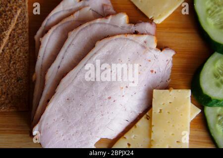 Affettare prosciutto, cetrioli e formaggio con pane ruddy sottile giace su un asse di legno. Foto Stock