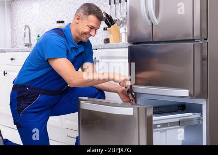 Maschio maturo del veterano della riparazione di un frigorifero con Toolbox in cucina Foto Stock