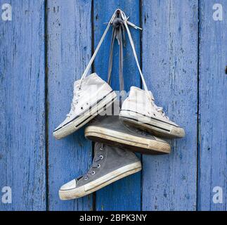 Due coppie di molto vecchio tessili usurati sneakers appendere su un chiodo, vecchio blu sullo sfondo di legno Foto Stock
