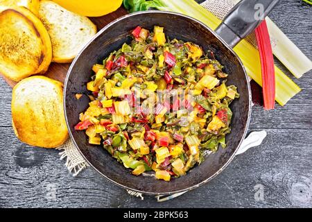 Warm bietole insalata con arancia e cipolla in una vecchia padella su un letto di sacco, pane, forcella su un nero lo sfondo di legno dal di sopra Foto Stock