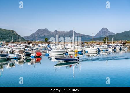 Nesna, Norvegia - 06 agosto 2019: Motoscafo guida di fronte alla marina di Nesna: Un sacco di barche a motore, barche a vela, barche di pescatori in blu calmo oc Foto Stock