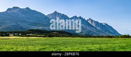 Vista panoramica su cinque delle montagne Seven Sisters di Sandnessjoen, idealmente verde erba, piccolo villaggio norvegese e montagne accanto al campo. S Foto Stock