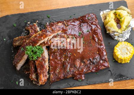 Grigliata di carne di maiale alla brace bimbo indietro nervature con patate al forno e alla griglia di mais dolce Foto Stock