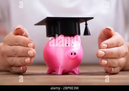 Close-up di una donna di mano la protezione di salvadanaio con graduazione il cappello sulla scrivania in legno Foto Stock