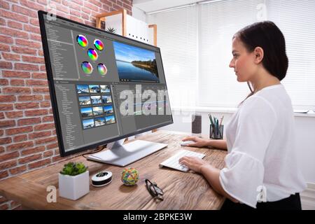 Vista laterale di Creative Editor femmina per editing video sul computer sulla scrivania in legno Foto Stock